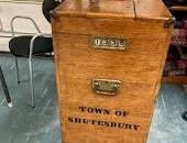 A wooden crank turn ballot box resting on a blue recycling bin